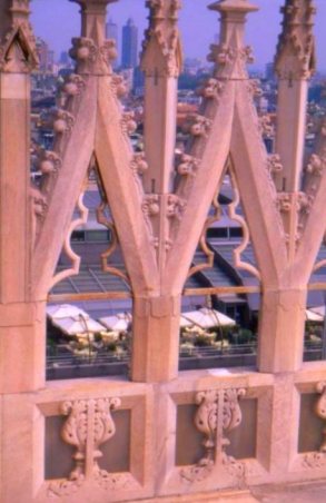 Downtown skyscrapers visible through stone lattice work, Duomo rooftop, Milano, Italy.